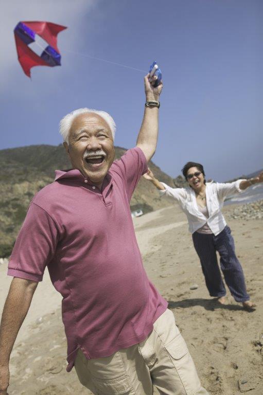 Retirement age couple at the beach flying a kite.